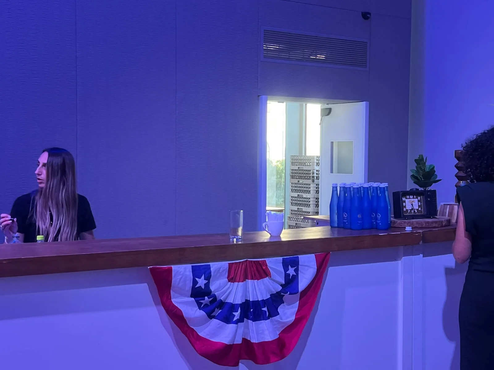 A row of blue Watergen glass bottles on a bar draped with red, white and blue bunting