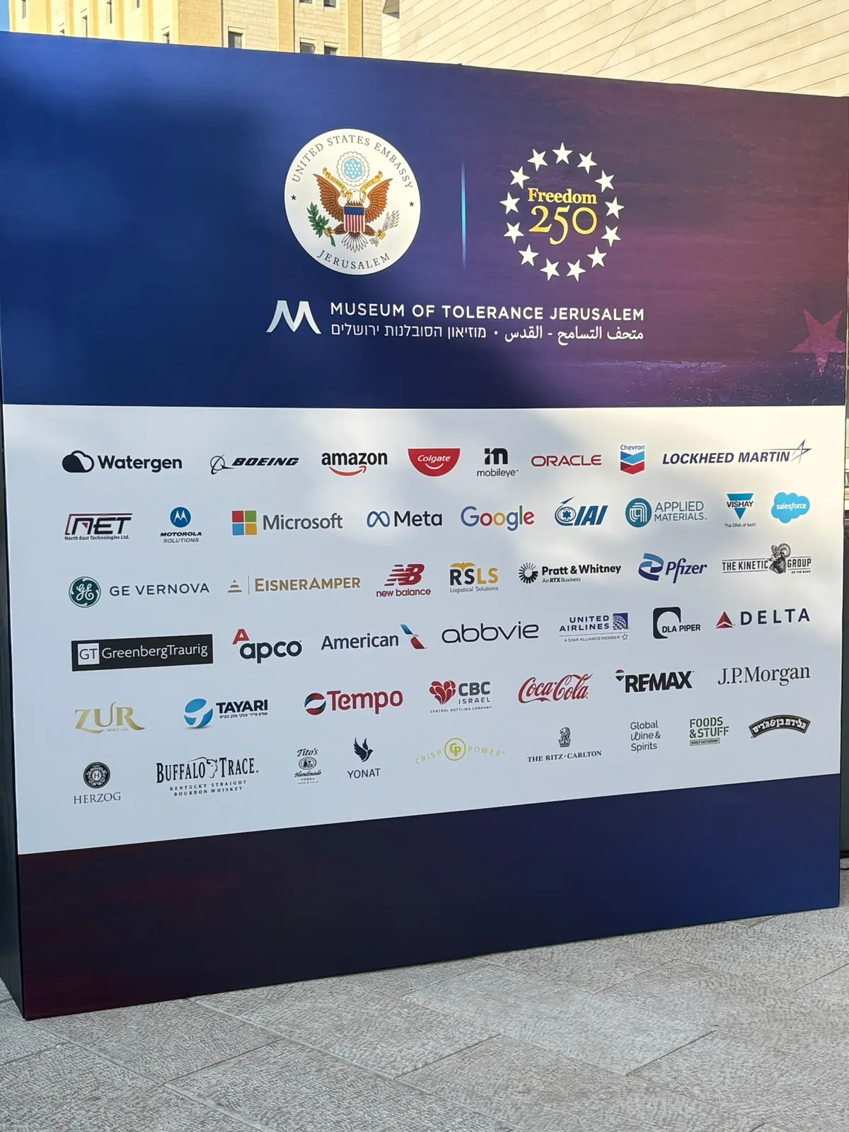 The Freedom 250 sponsor wall with the U.S. Embassy seal, Watergen first among the logos beside Boeing, Amazon, Google and Microsoft