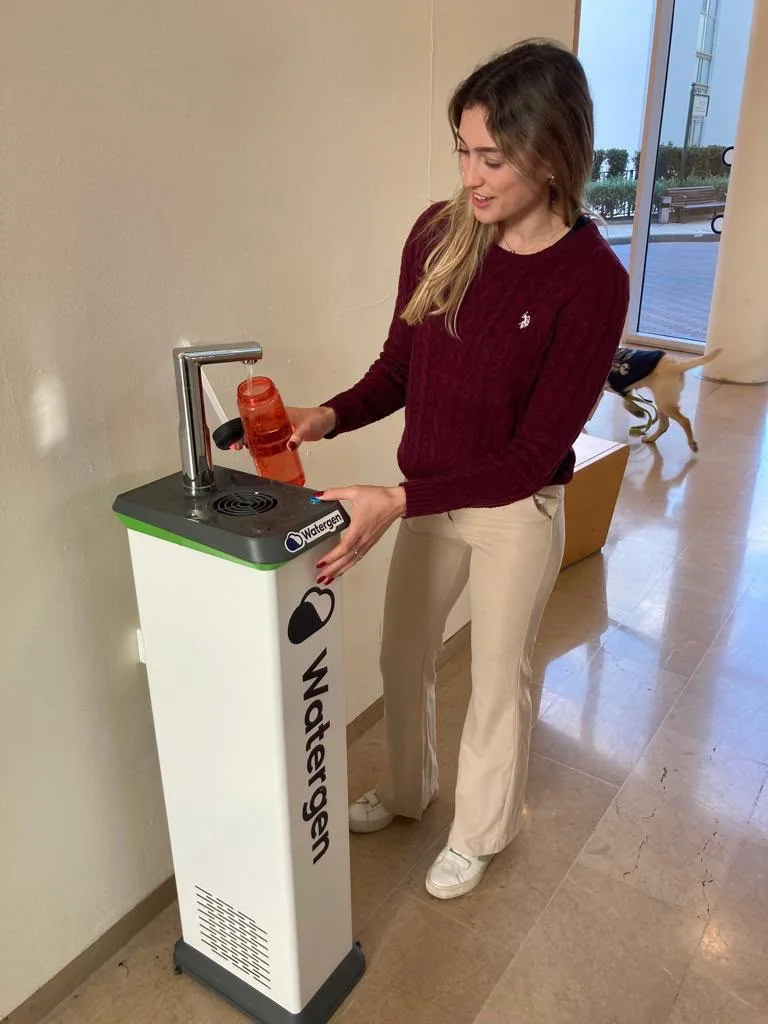 A student filling a reusable bottle at a Watergen dispenser in a campus lobby