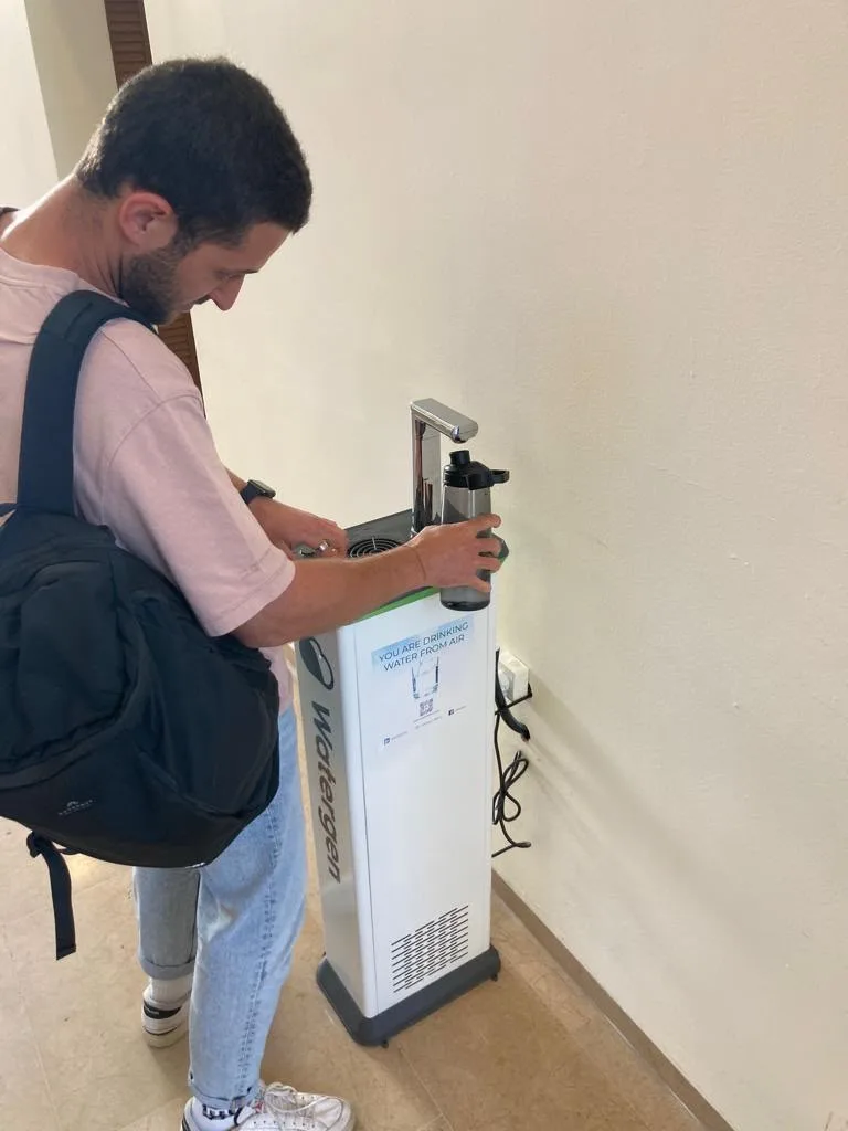 A student refilling a bottle at a Watergen dispenser marked “You are drinking water from air”