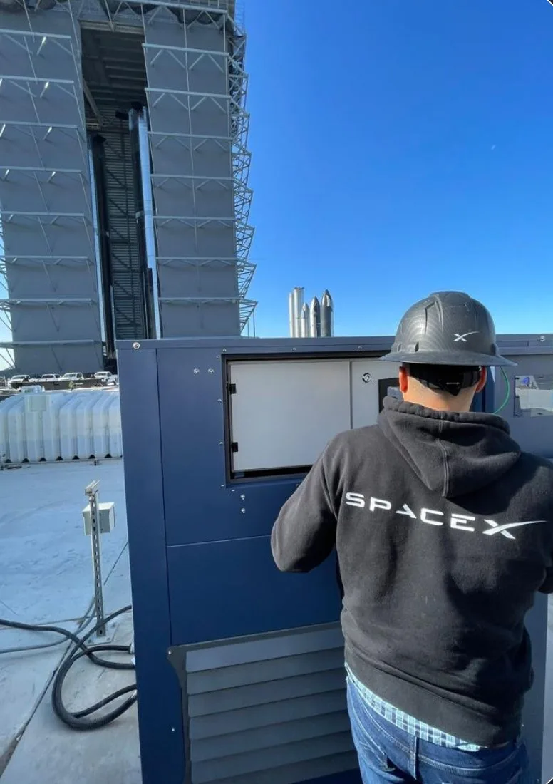 A SpaceX technician working at a Watergen unit, the launch tower and Starship vehicles behind