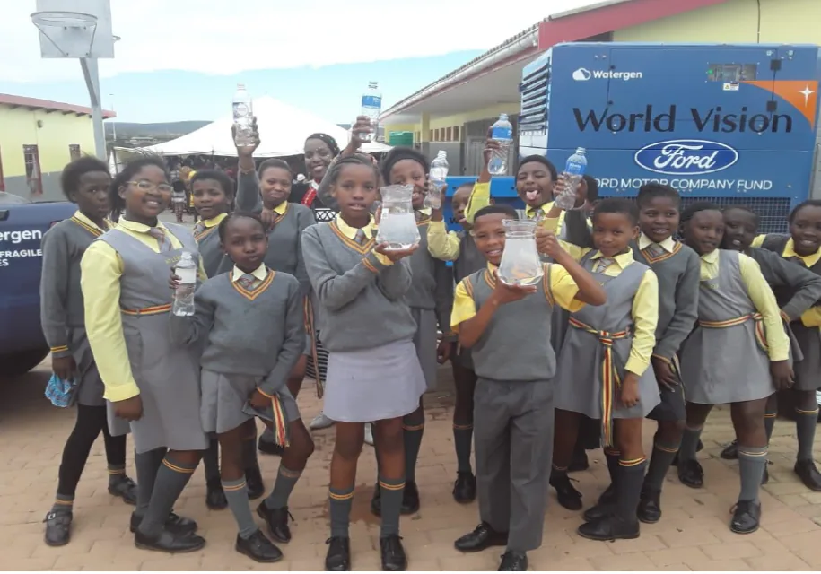 Schoolchildren holding cups of water in front of a World Vision Watergen trailer in South Africa