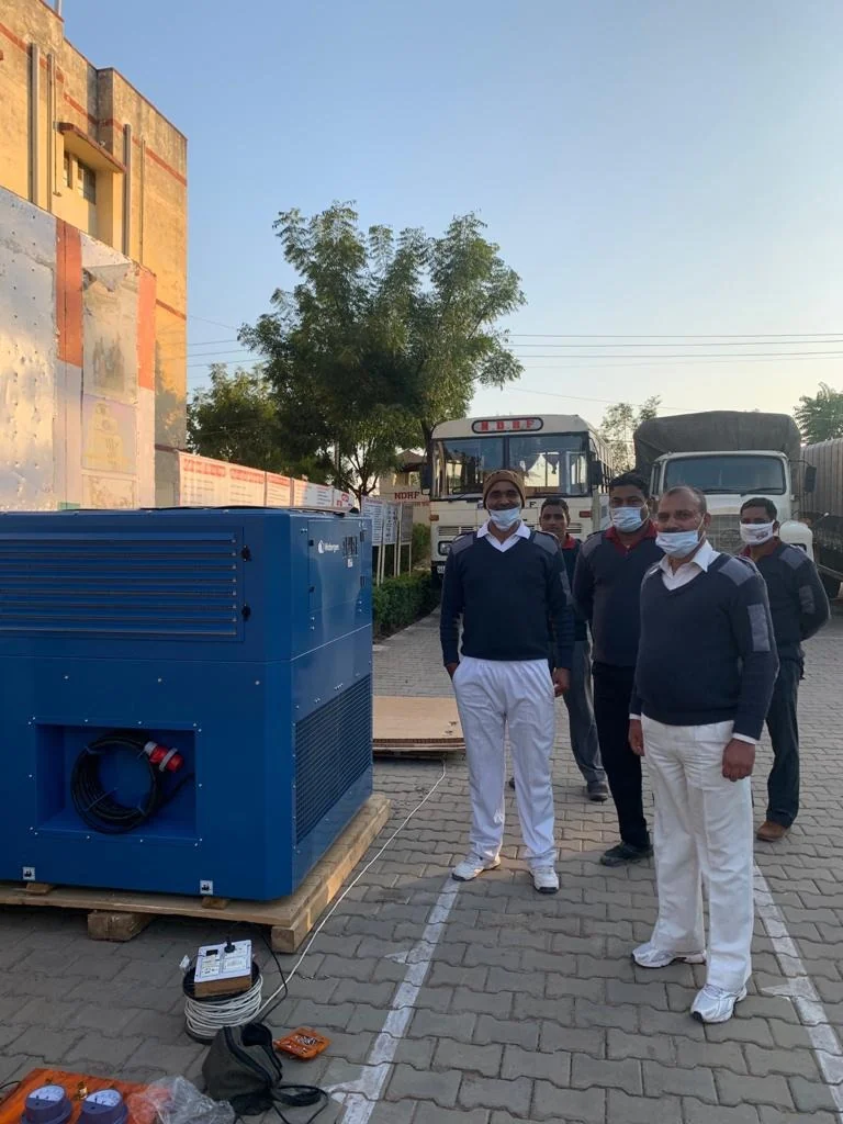 An Indian disaster-response crew beside a palletized Watergen unit with their trucks behind