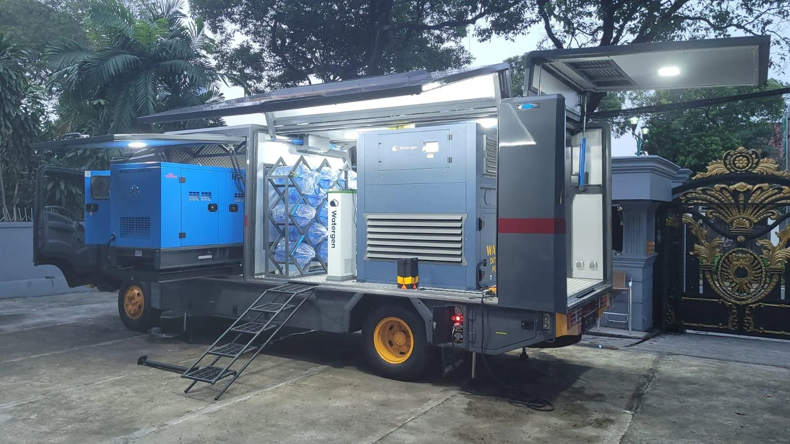 A mobile Watergen water truck with fold-out sides revealing a generator, a rack of water jugs and a dispenser